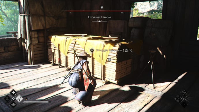 Naoe in Assassin's Creed Shadows crouches next to a resource stockpile inside a wooden building.