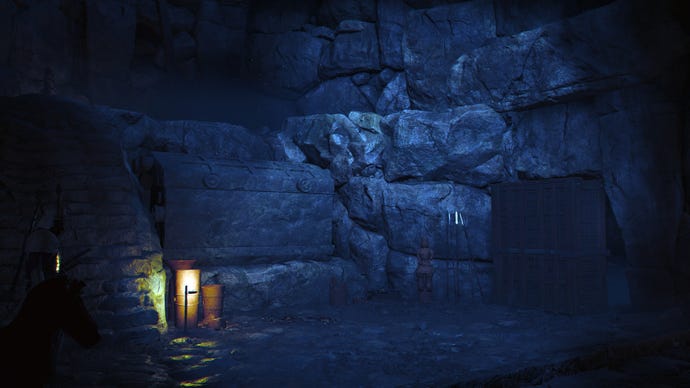 The interior of a kofun in Assassin's Creed Shadows. It is dark, with a small lantern light the only illumination. A large chest can be seen amongst the gloom.