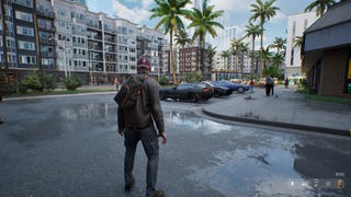 A man in a hoody stands on wet asphalt with a row of cars ahead of him and palm trees in the distance.