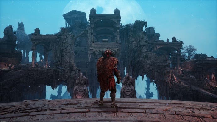 The player wears a red cape and stands atop a platform looking at some ruins.